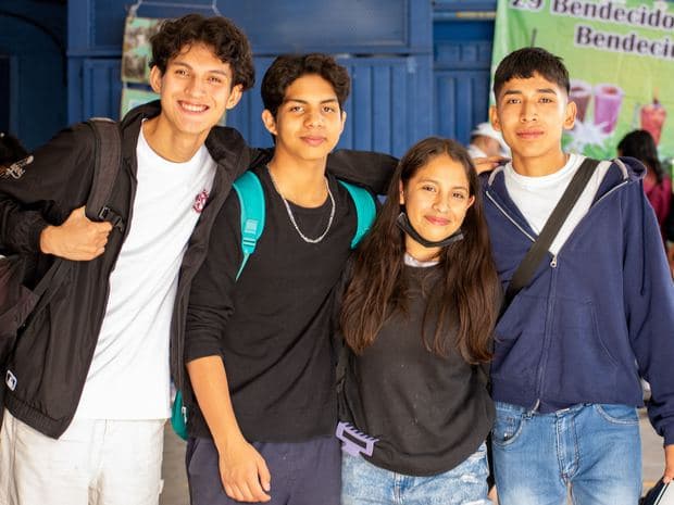 Four students arm in arm outside school.