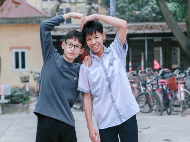 Two friends standing together outside, one with an arm raised overhead.